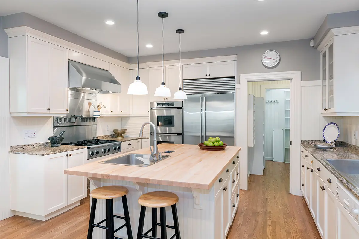 Bright and modern kitchen painted by Dream Painting, featuring white cabinets, a wooden island, stainless steel appliances, and pendant lighting.