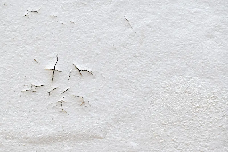 Wall with cracks and peeling paint showing surface damage on a white textured finish.