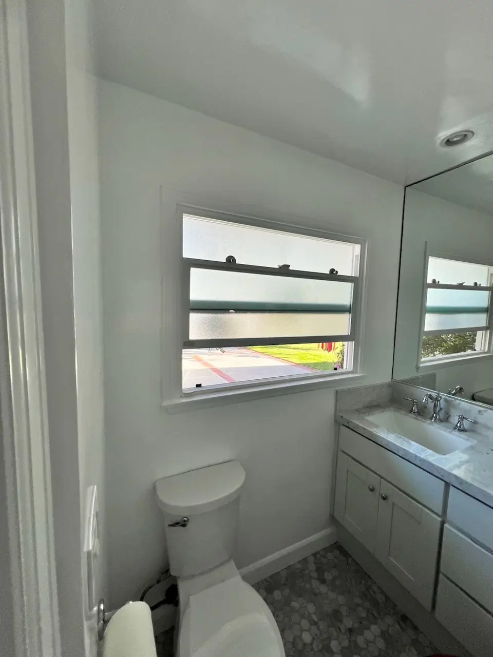 Bathroom wall in Costa Mesa after renovation, featuring freshly painted walls, a window, modern sink vanity, and a clean toilet with polished fixtures.